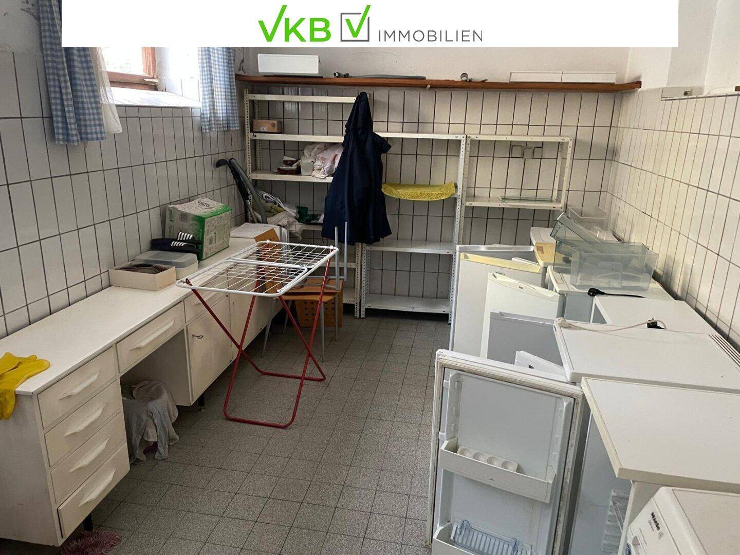 Waschküche oder Abstellraum mit Fliesenboden, Regalen und mehreren Kühlschränken, funktional ausgestattet.