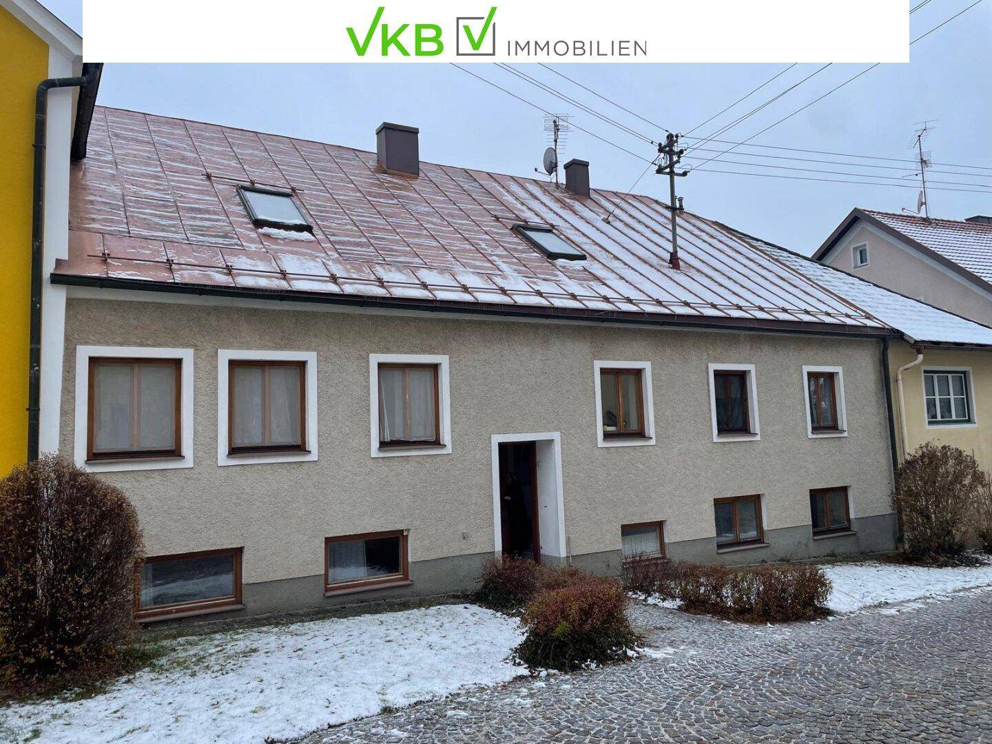 Rückansicht eines Wohnhauses mit mehreren Fenstern und einem Ziegeldach, umgeben von Schnee.