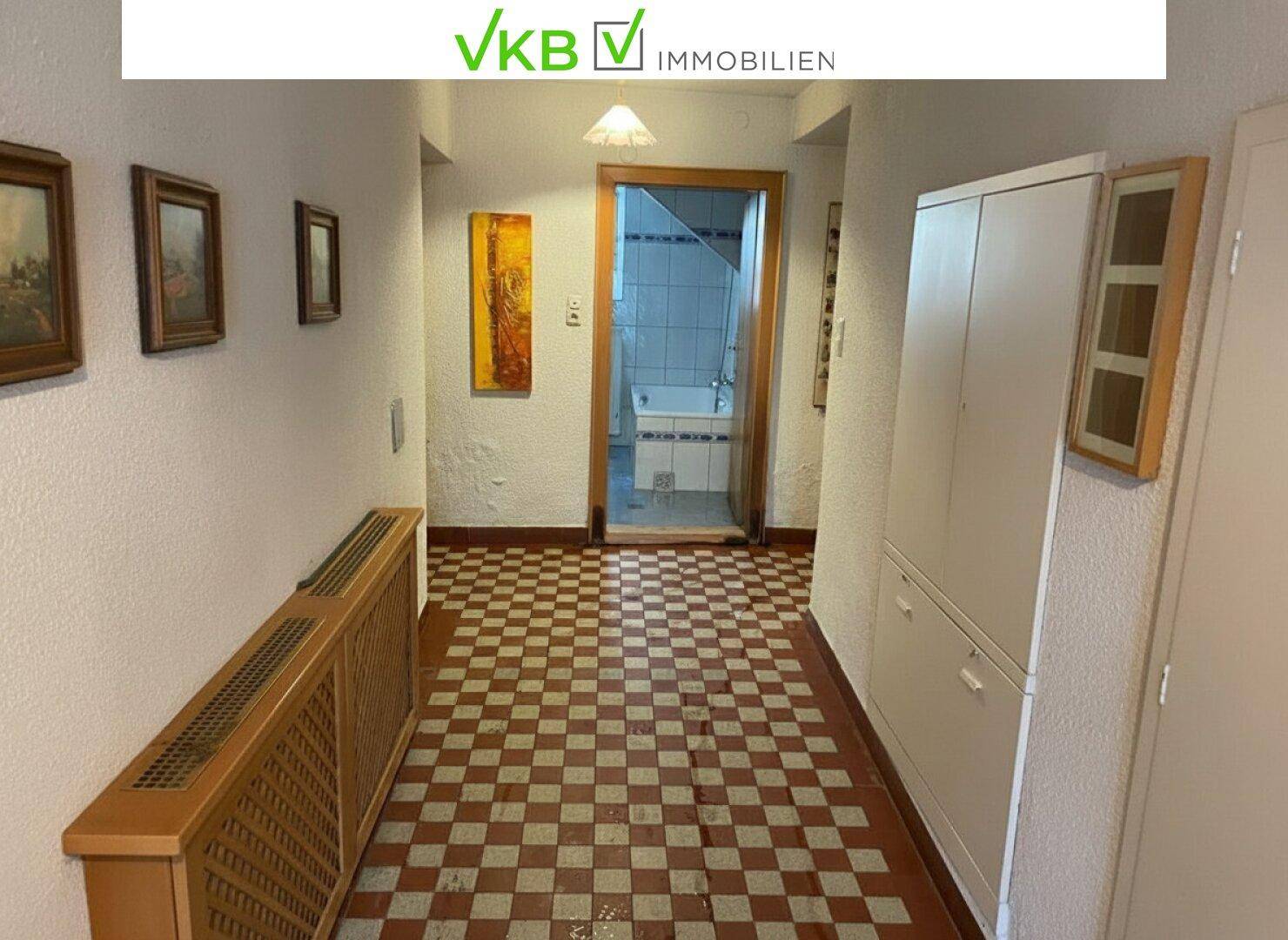 Flur mit kariertem Fliesenboden, Wandschrank und Bildern an der Wand, führt zu einem Badezimmer.