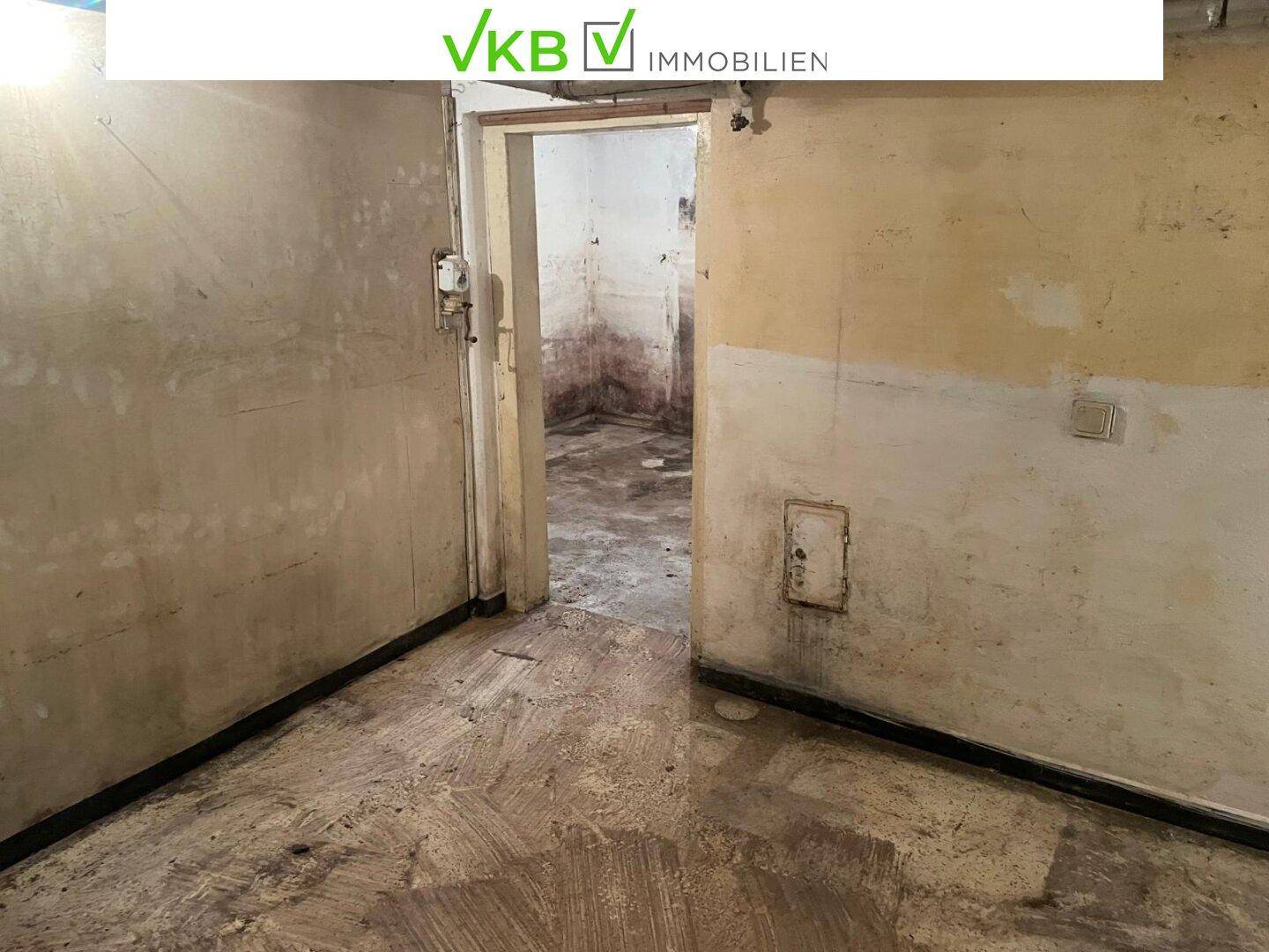 Unfertiger Kellerraum mit Betonboden und Zugang zu weiteren Bereichen.