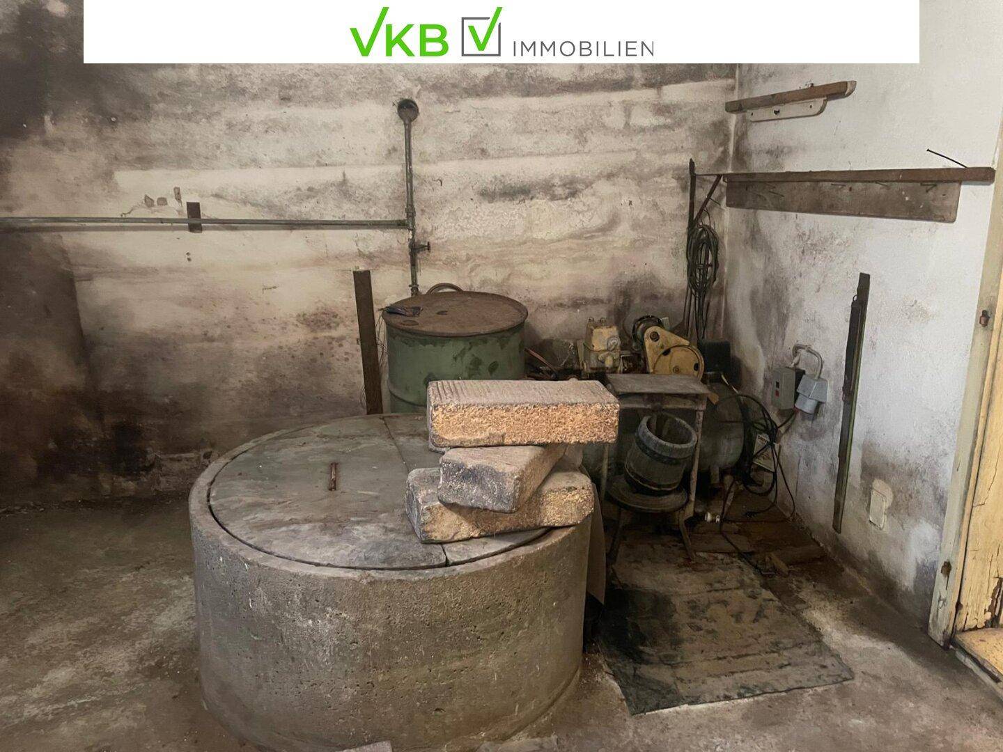 Kellerraum mit Brunnenabdeckung und verschiedenen Geräten, dient als Technikbereich.