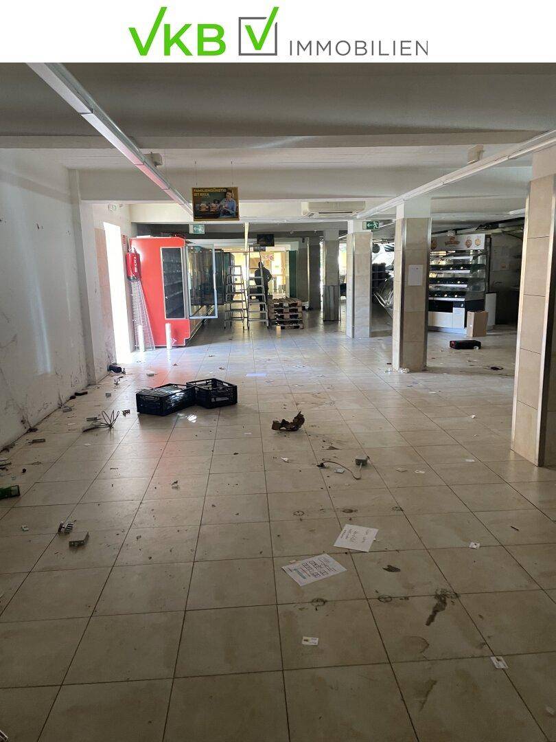 Großer, leerstehender Ladenbereich mit Fliesenboden und sichtbaren Deckenstrukturen, bereit für Renovierung.