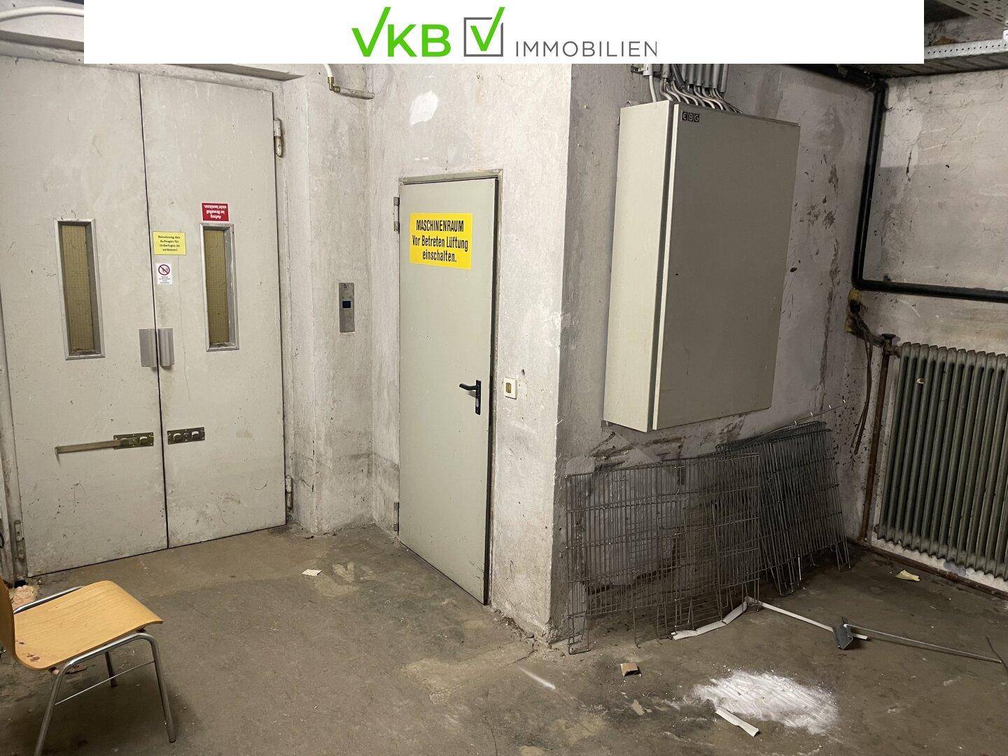 Bereich mit Aufzugstüren und einem Schild zum Maschinenraum, umgeben von Betonwänden.