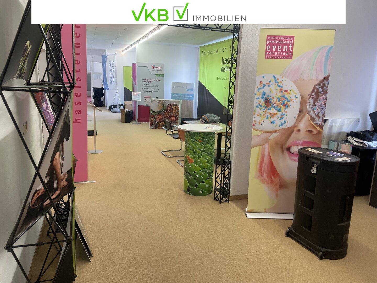 Großer Veranstaltungsraum mit Teppichboden und verschiedenen Werbebannern und Ausstellungsständen.
