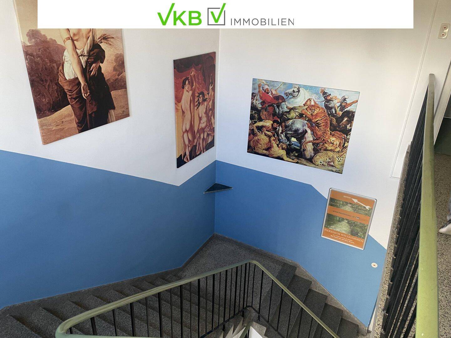 Treppenhaus von oben gesehen mit blau-weißen Wänden, Kunstwerken und einem Terrazzoboden.