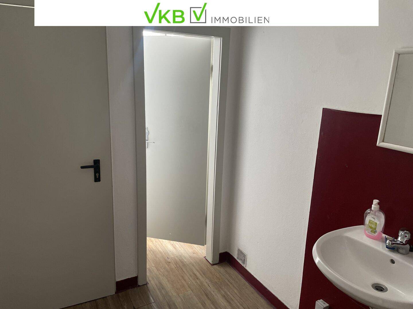 Kleiner Raum mit Waschbecken und Holzboden, möglicherweise eine Gästetoilette oder ein Abstellraum.