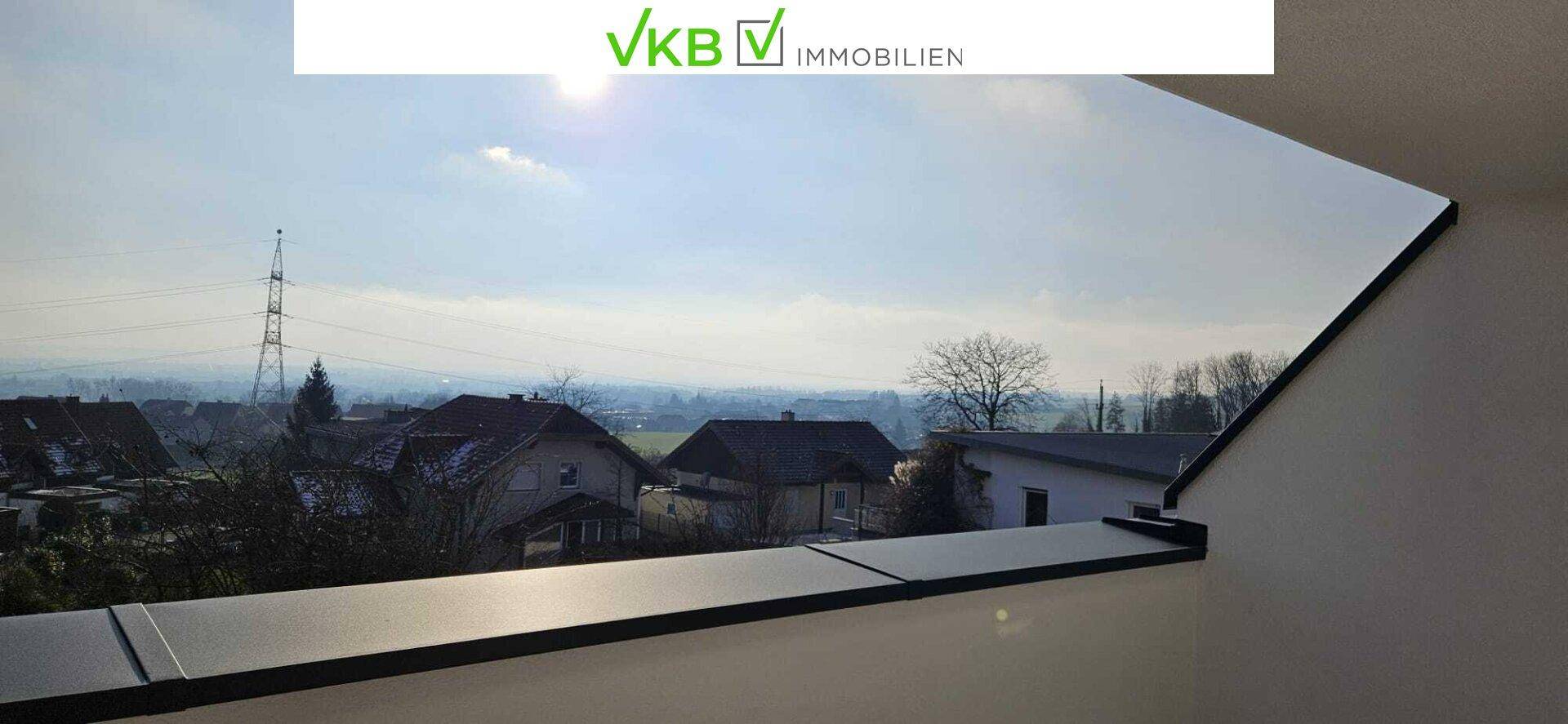 Weitblick über die Landschaft mit Häusern und einem Strommast unter hellem Himmel.