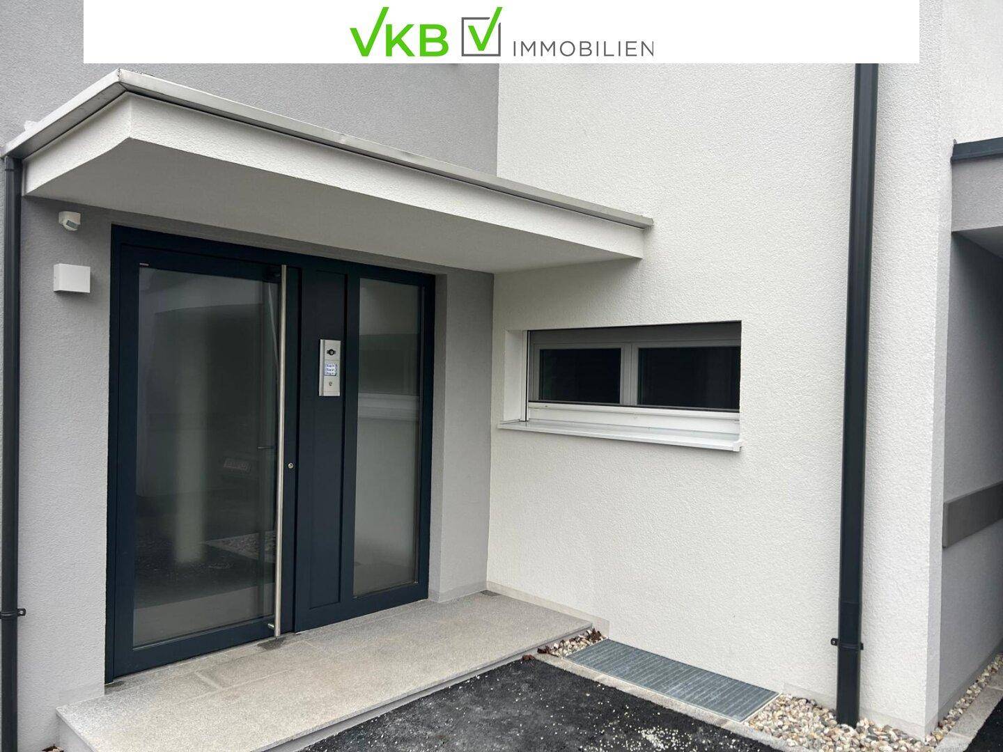 Moderner Eingangsbereich eines Gebäudes mit dunkler Tür und kleinerem Fenster.
