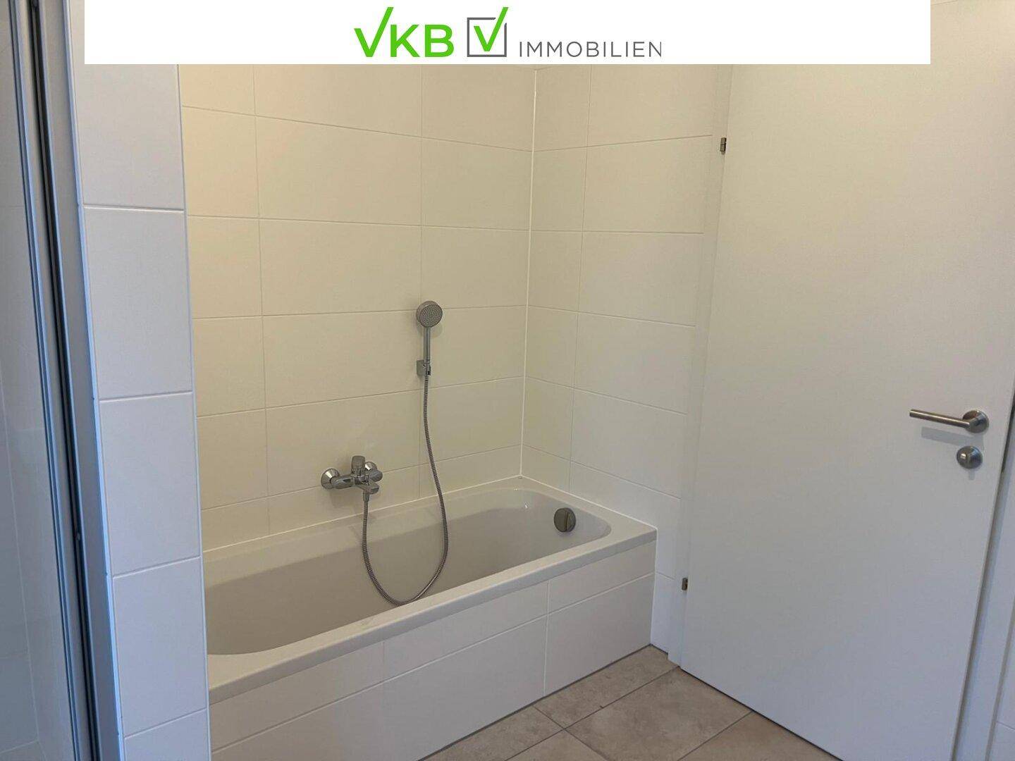 Badezimmer mit weißen Fliesen und einer integrierten Badewanne.