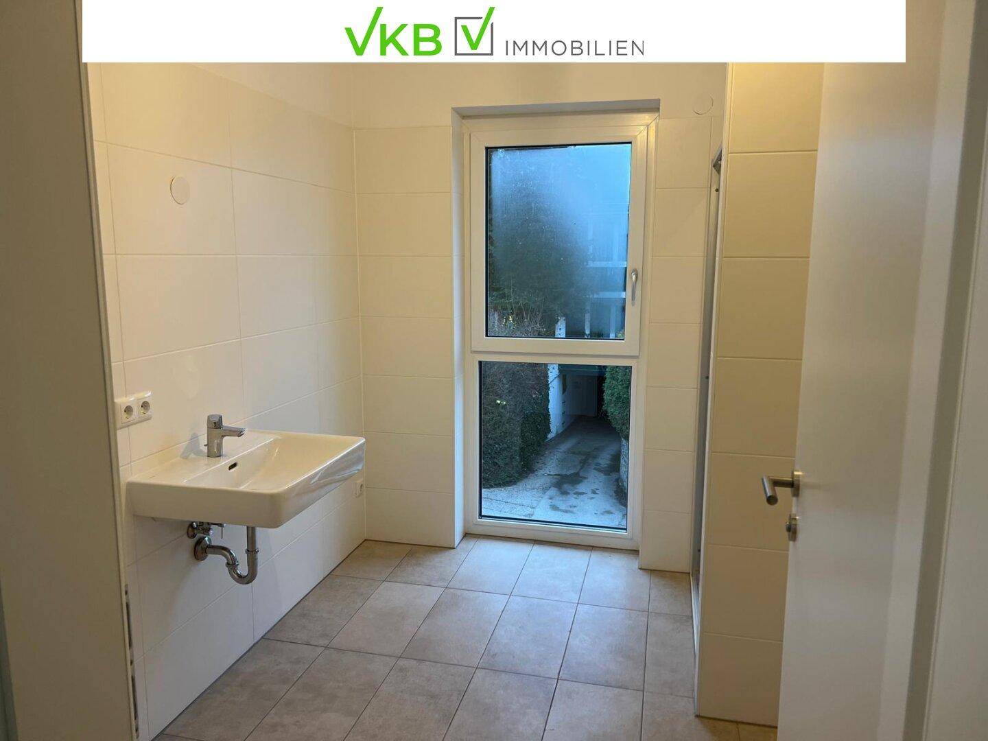Helles Badezimmer mit weißen Fliesen, Waschbecken und einem Fenster.