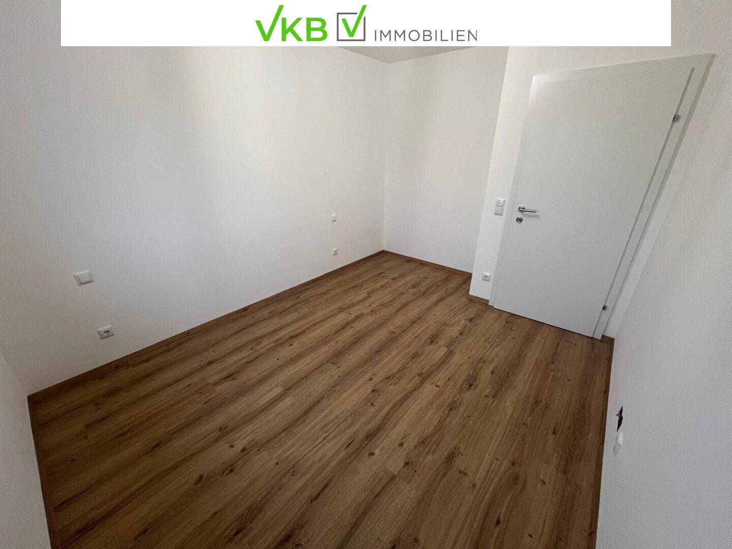 Leeres Zimmer mit Holzboden und weißer Tür, bereit für die Einrichtung.