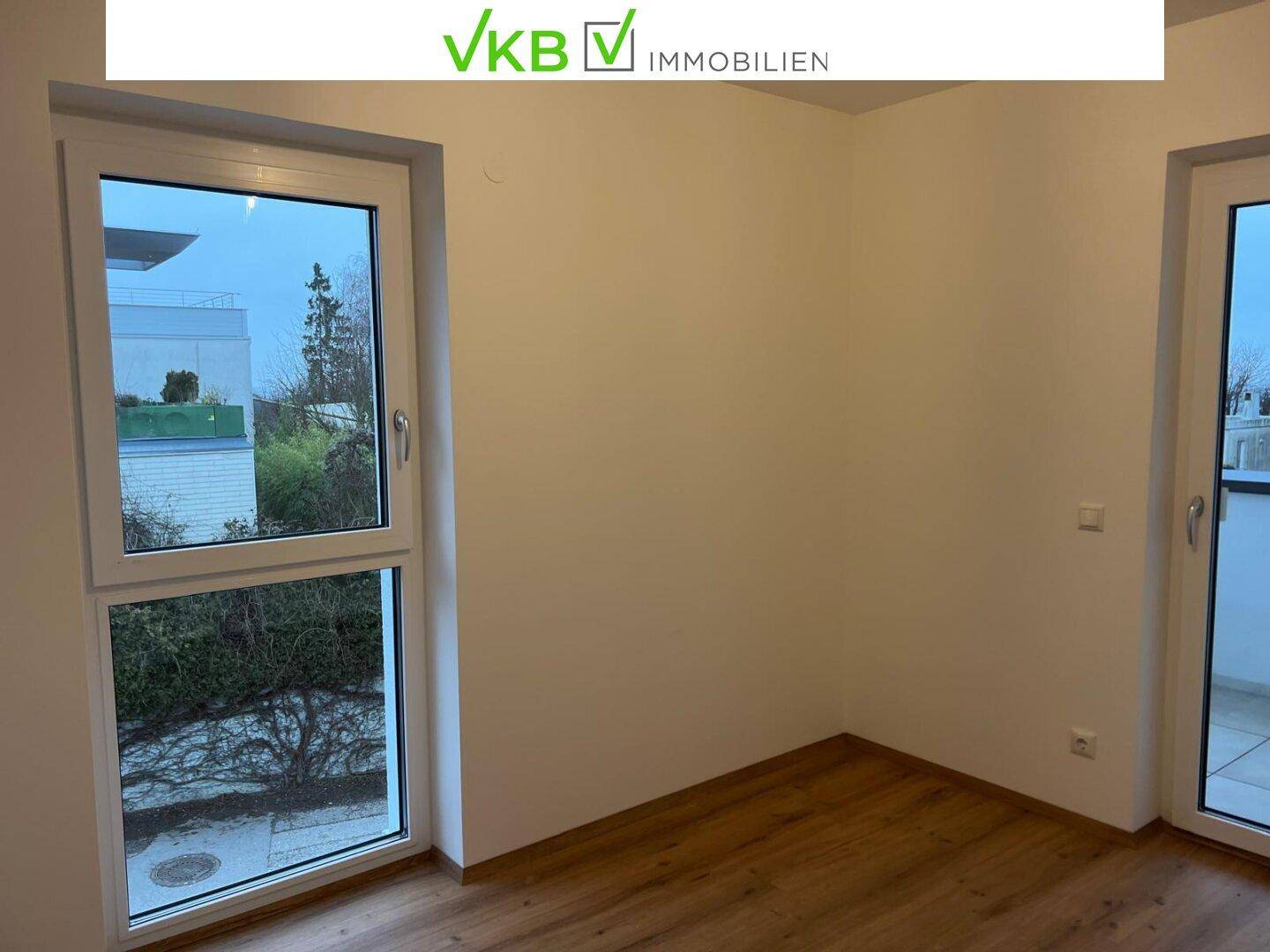 Helles Zimmer mit Holzboden und zwei großen Fenstern, bereit zur individuellen Gestaltung.