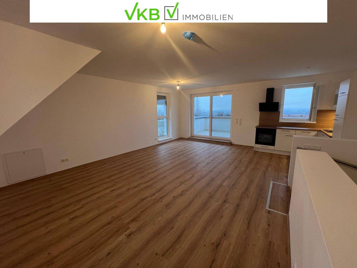 Großzügiger offener Wohn- und Küchenbereich mit Holzboden und Zugang zum Balkon.