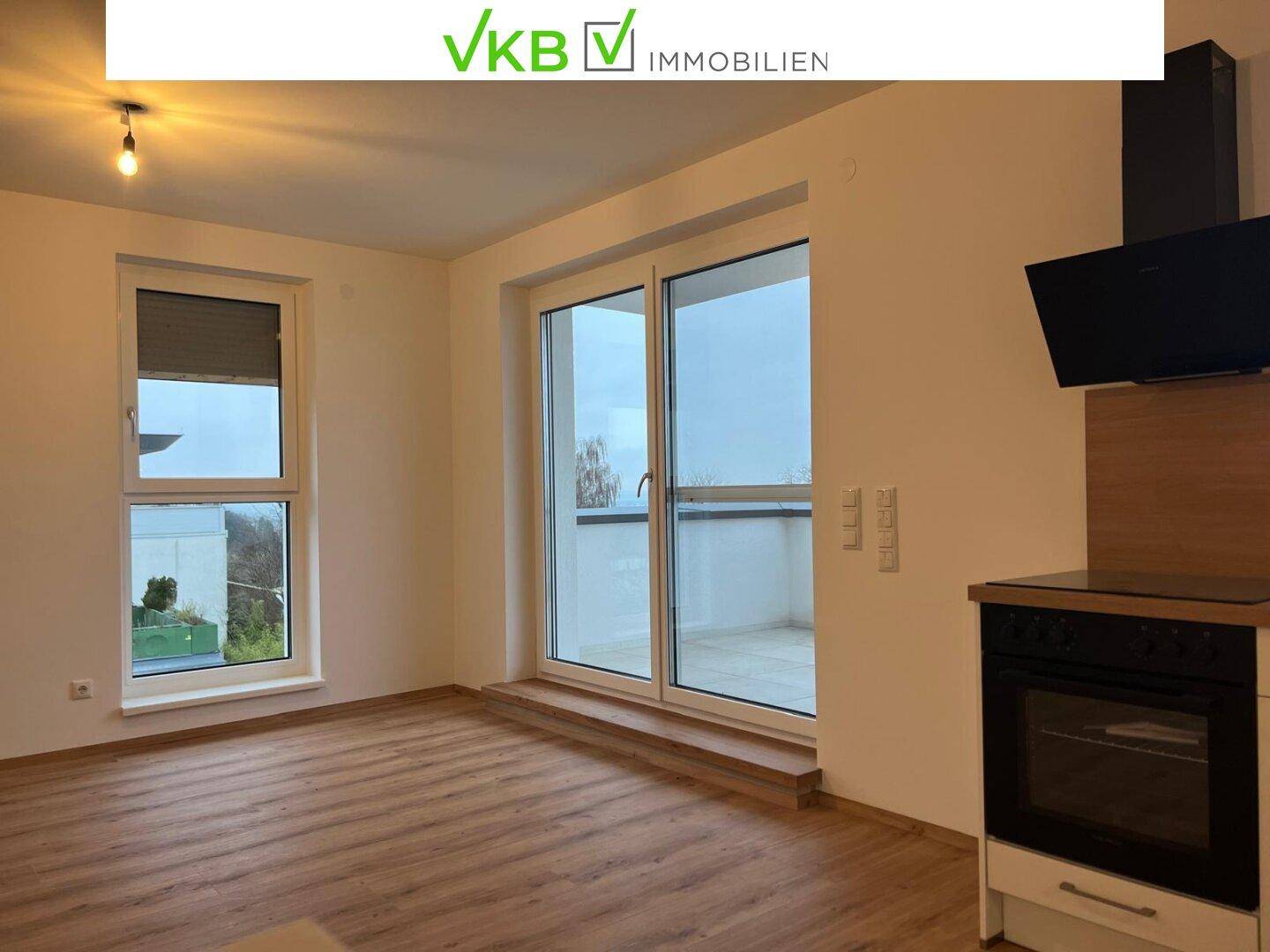 Heller Wohnbereich mit Holzboden, großen Fenstern und Zugang zu einem Balkon.
