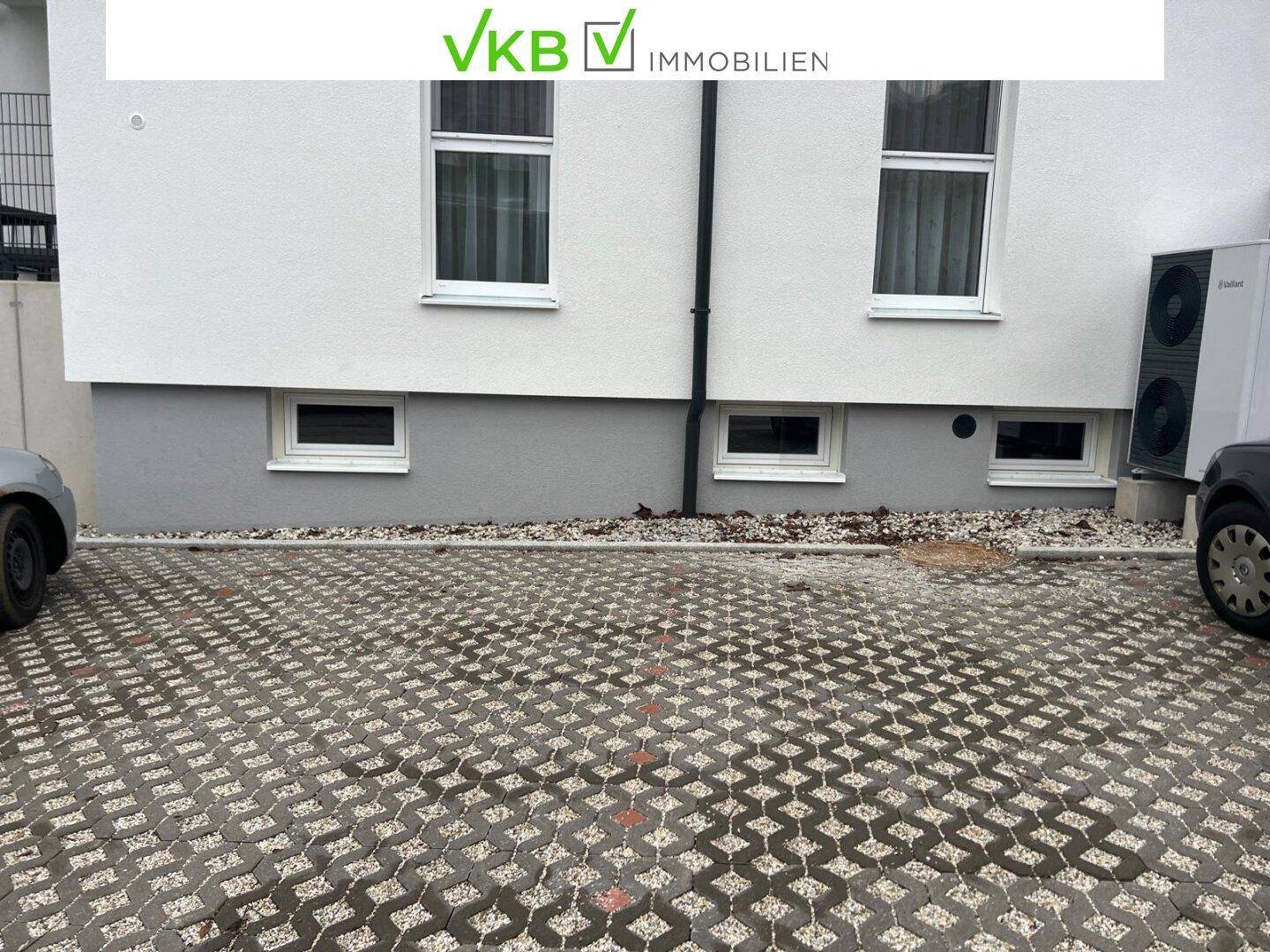 Außenansicht des Gebäudes mit Parkplatz aus Rasengittersteinen und einer Wärmepumpe.