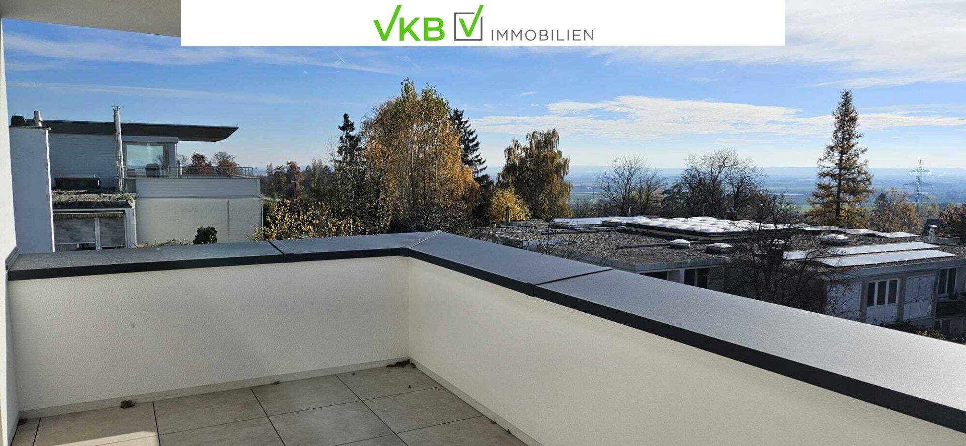 Geräumige, geflieste Terrasse mit weißer Brüstung und Blick auf Bäume und umliegende Gebäude.