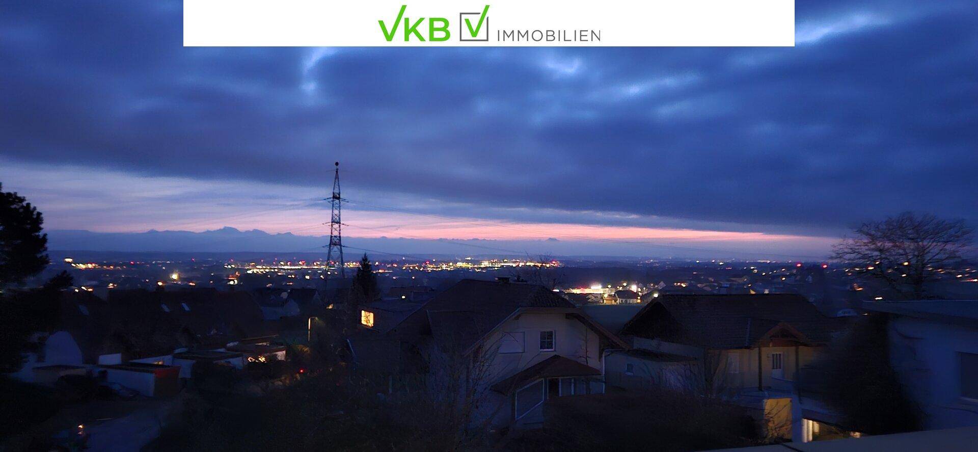 Nächtlicher Panoramablick über die beleuchtete Stadt und die fernen Berge.