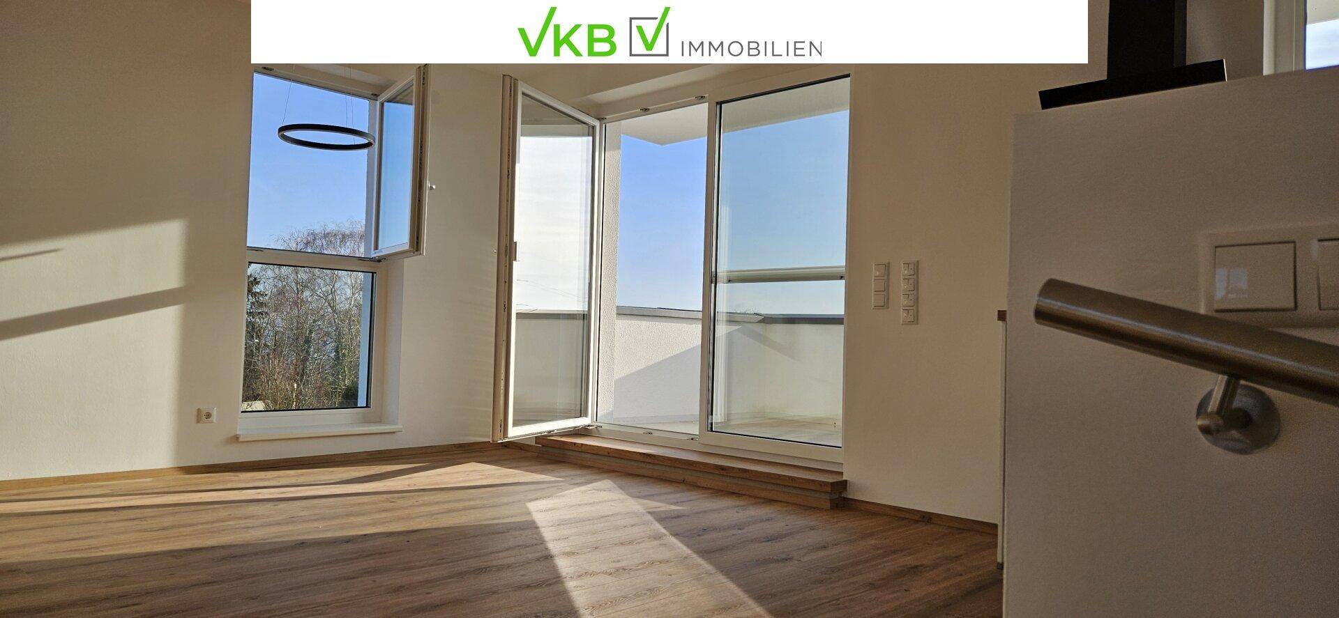 Lichtdurchfluteter Wohnbereich mit Holzboden, großen Fenstern und offenem Zugang zum Balkon.