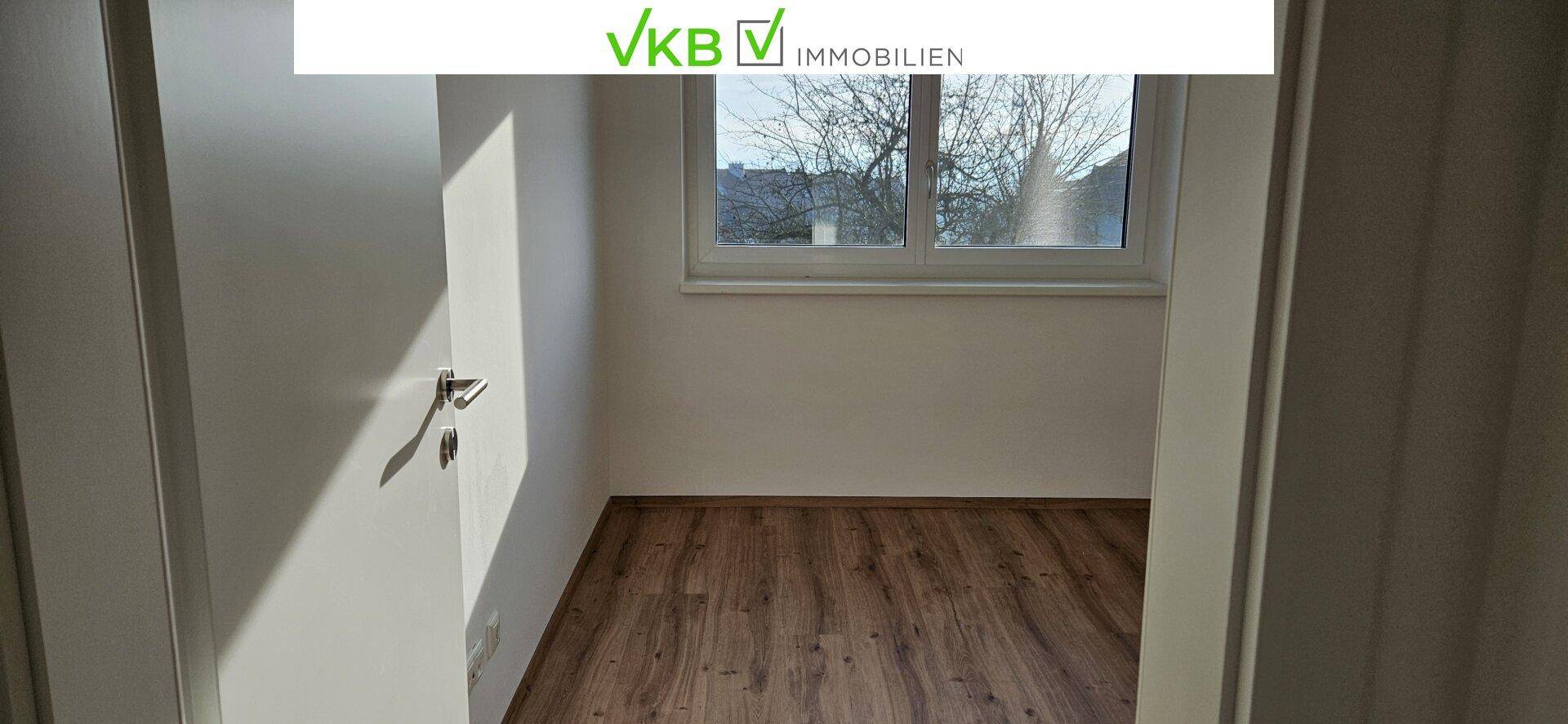 Helles Zimmer mit Holzboden und Fenster, gesehen durch einen Türrahmen.