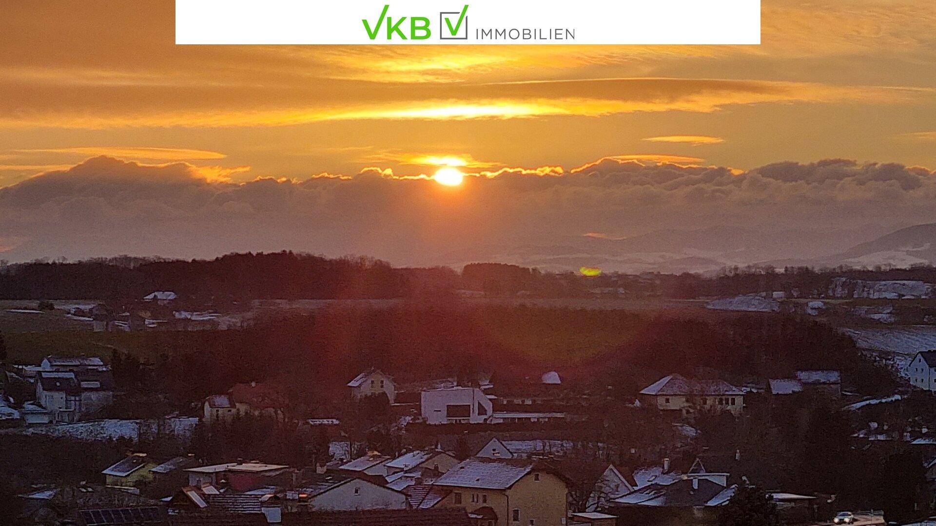 Weitblick über eine verschneite Landschaft mit Häusern und einem strahlenden Sonnenaufgang über den Bergen.