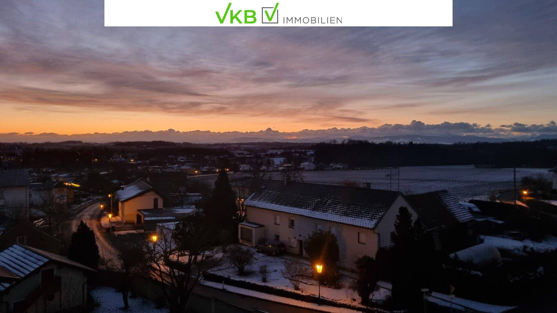 Abendlicher Blick über eine verschneite Siedlung und Felder mit beleuchteten Straßenlaternen.