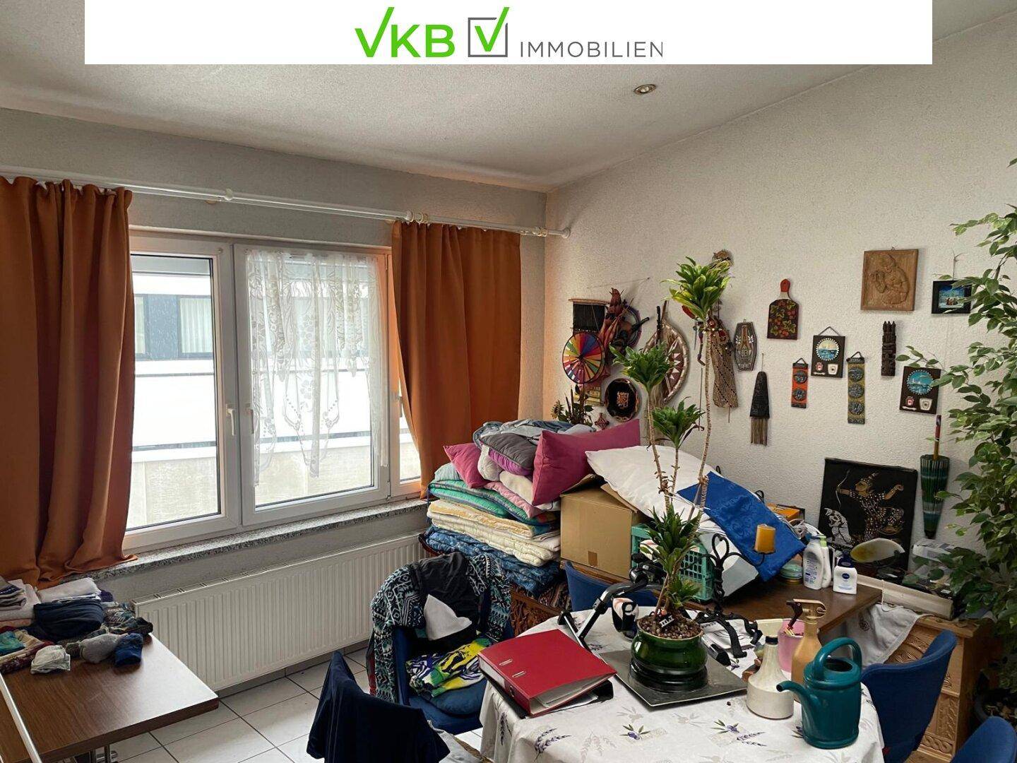 Wohnbereich mit großem Fenster, Vorhängen und einem Esstisch, umgeben von Pflanzen.