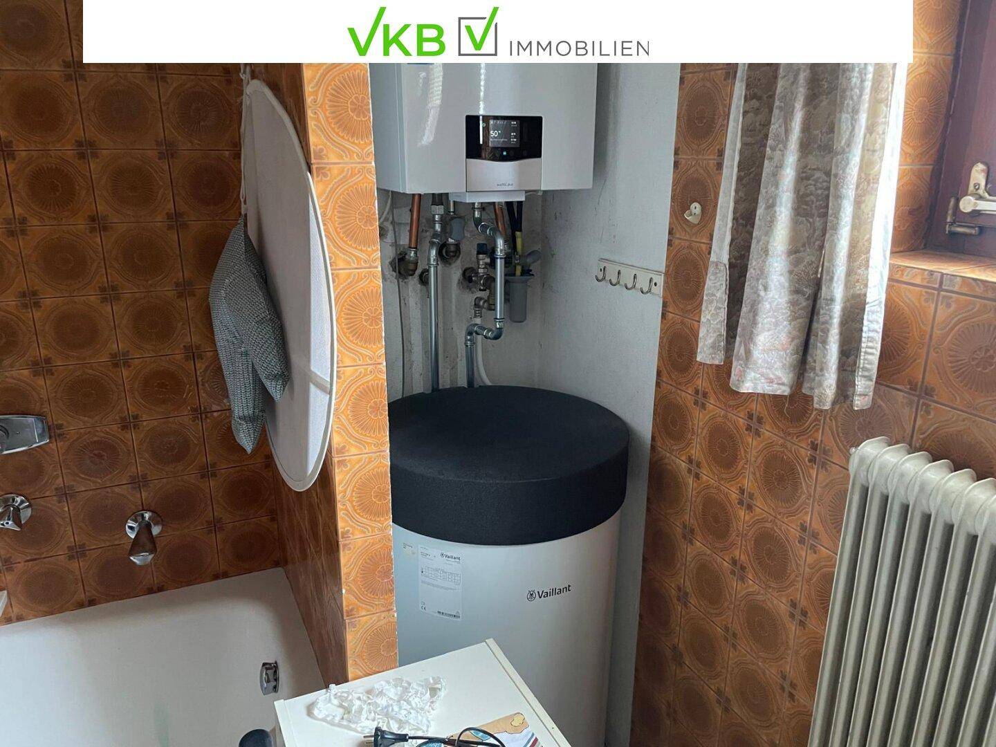 Nahaufnahme eines modernen Warmwasserbereiters in einem Badezimmer mit braunen Fliesen.