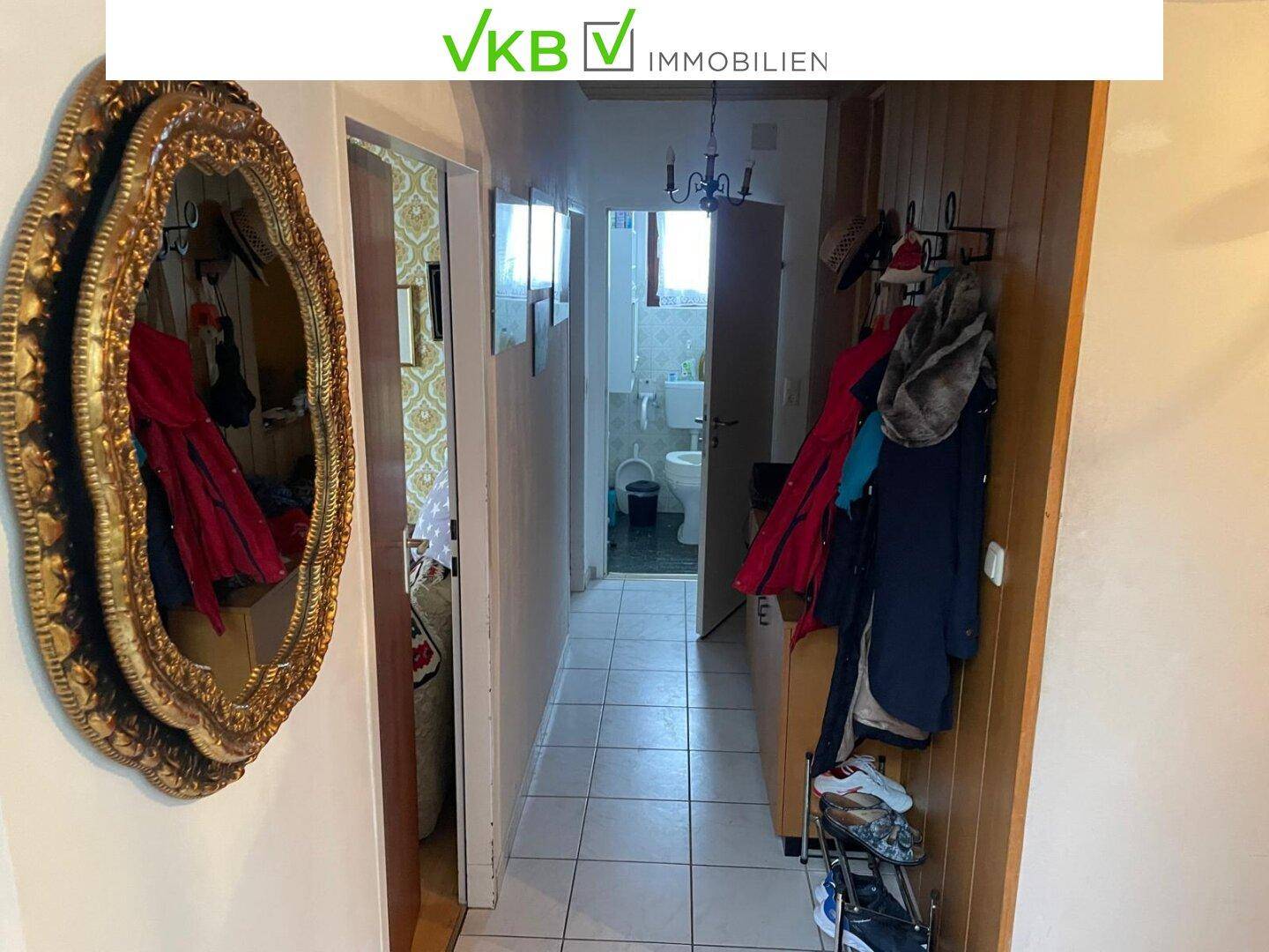 Flur mit Fliesenboden, Spiegel und Garderobe, der zu einem Badezimmer führt.