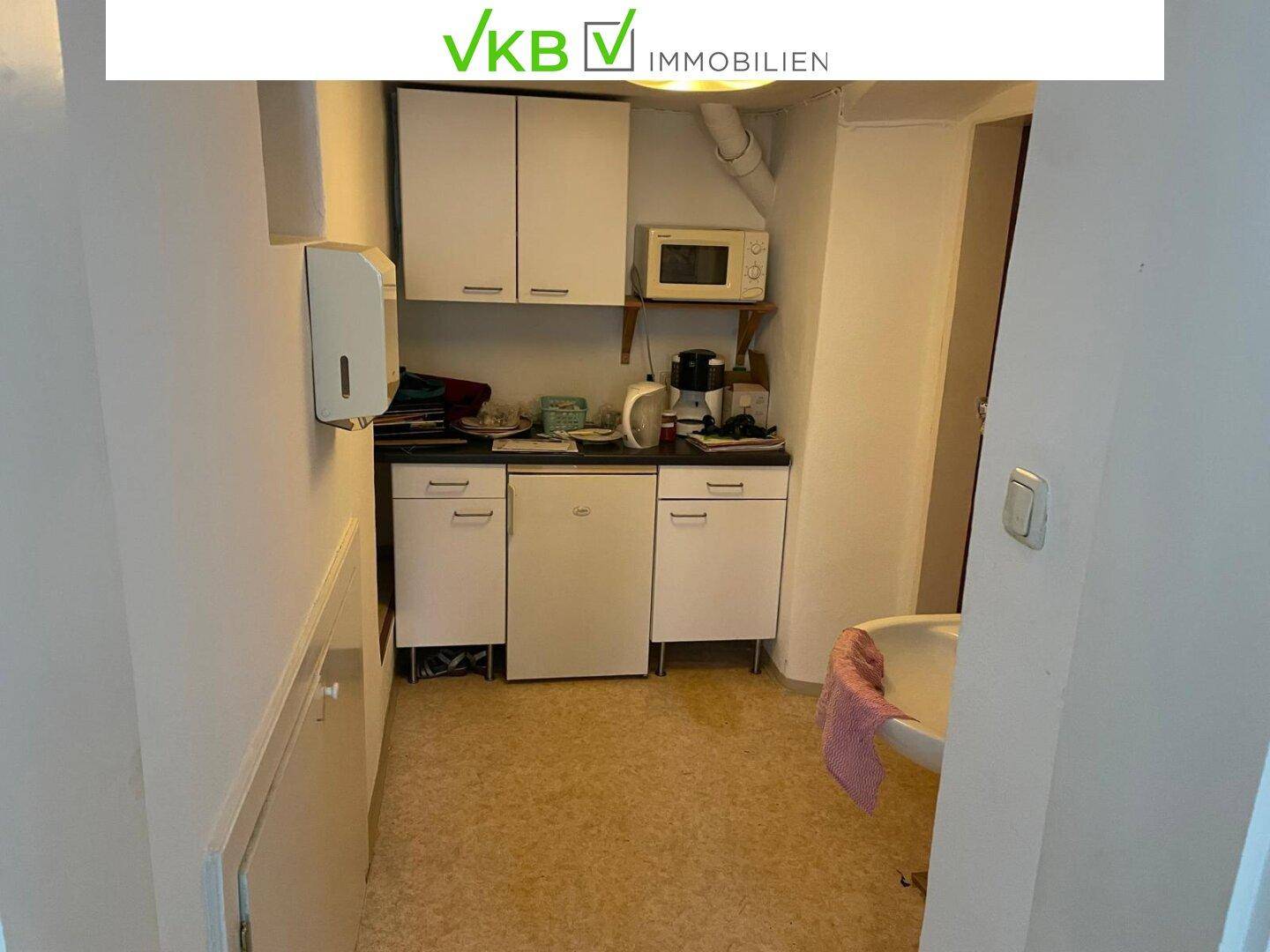 Kleine Küchenzeile mit weißen Schränken, Mikrowelle und Spülbecken in einem schmalen Raum.