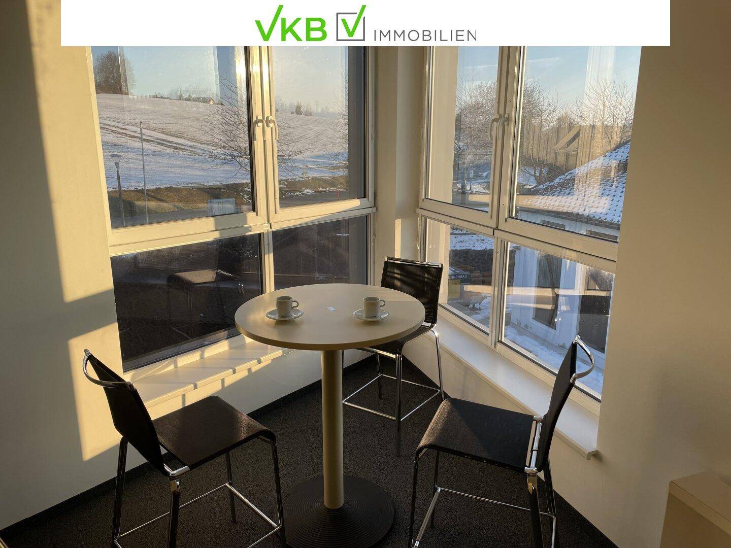 Gemütliche Sitzecke mit kleinem Tisch und Stühlen, umgeben von großen Fenstern mit Blick auf die verschneite Landschaft.