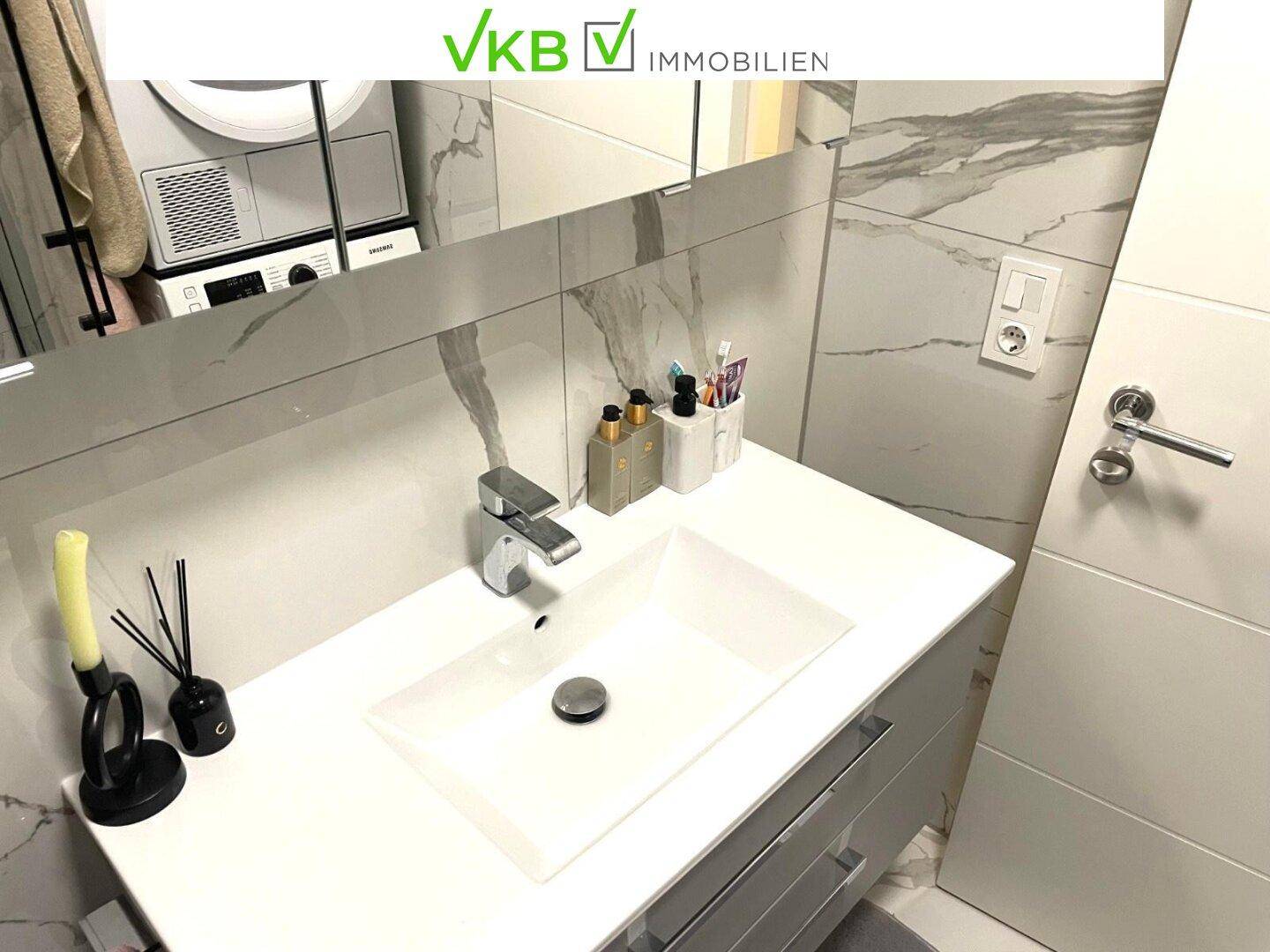 Badezimmer mit elegantem Einzelwaschbecken, großem Spiegel und Marmoroptik-Fliesen.