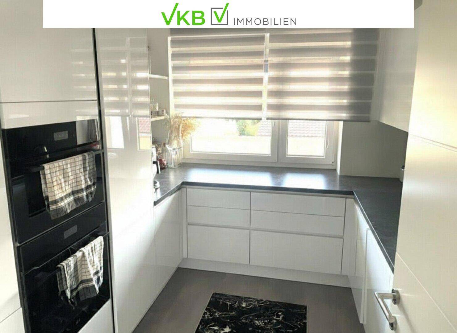 Moderne Küche mit weißen Schränken, dunkler Arbeitsplatte und Fenster.