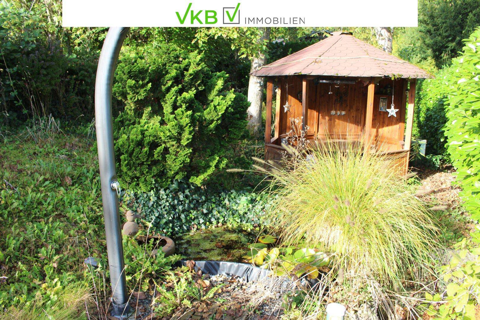 Idyllischer Gartenbereich mit einem Holzpavillon, einem kleinen Teich und einer Außendusche.
