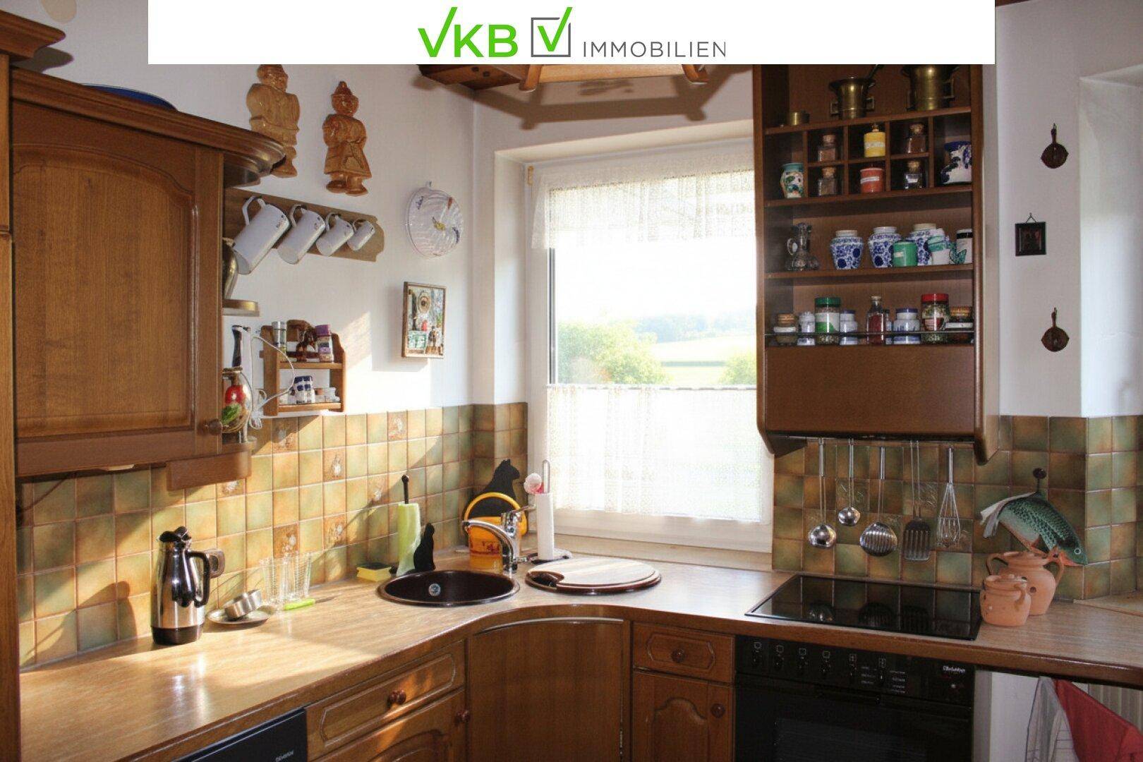 Traditionelle Holzküche mit gefliestem Fliesenspiegel und Blick ins Grüne durch das Fenster.