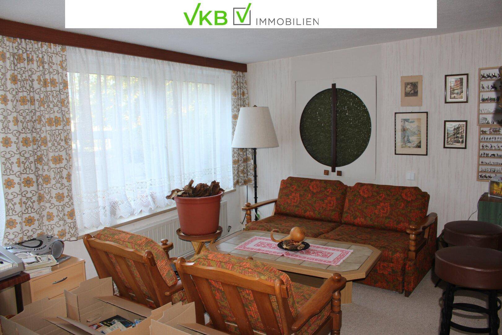 Gemütliches Wohnzimmer mit floralen Vorhängen, Sofa und Sesseln im Vintage-Stil.