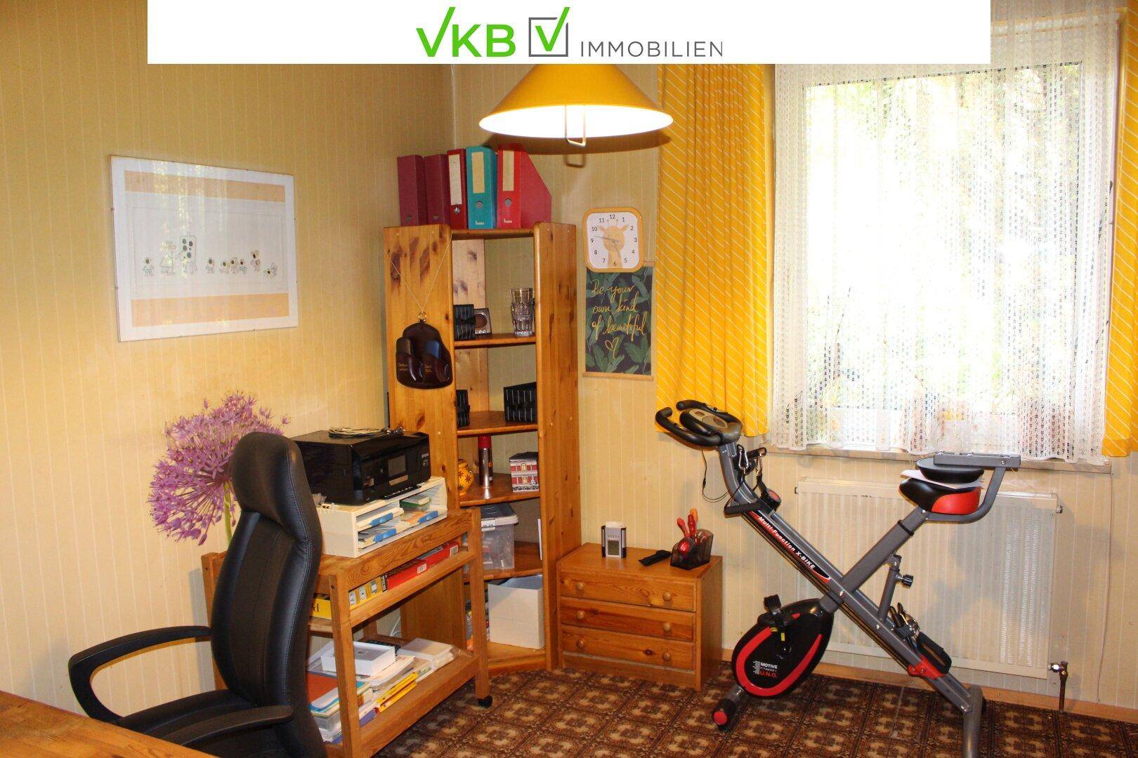 Helles Zimmer mit Schreibtisch, Regal und Heimtrainer, ideal als Büro oder Hobbyraum.