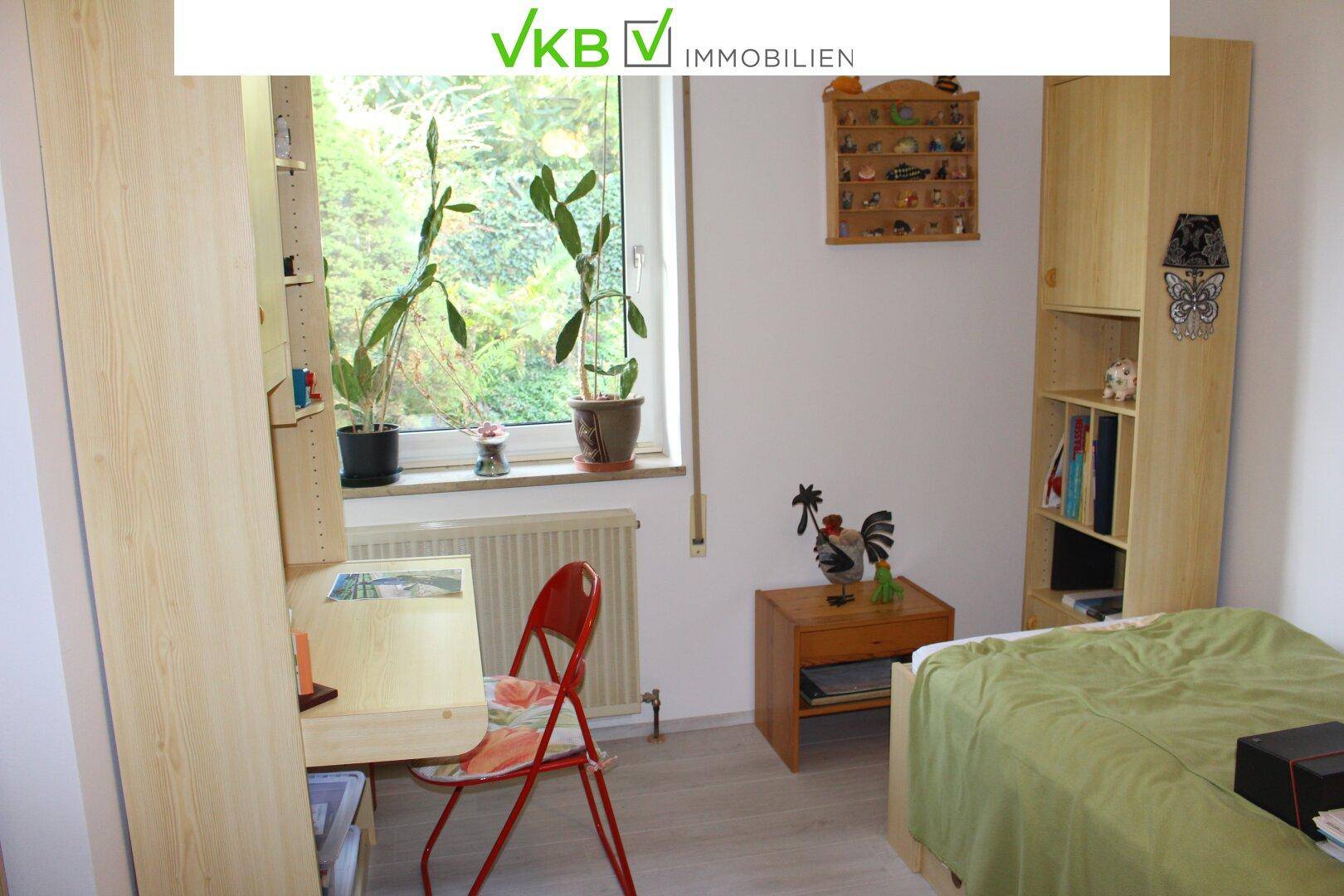 Helles Schlafzimmer mit Einzelbett, Schreibtisch und Fenster mit Blick ins Grüne.