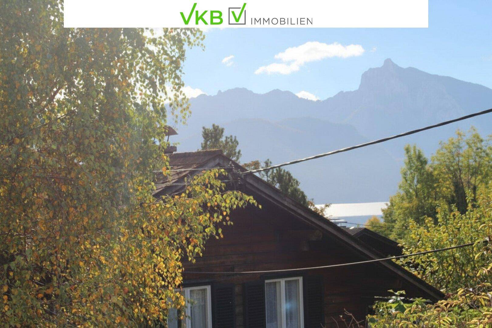 Malerischer Blick auf Berge und einen See, umgeben von herbstlichen Bäumen und einem Holzdach.
