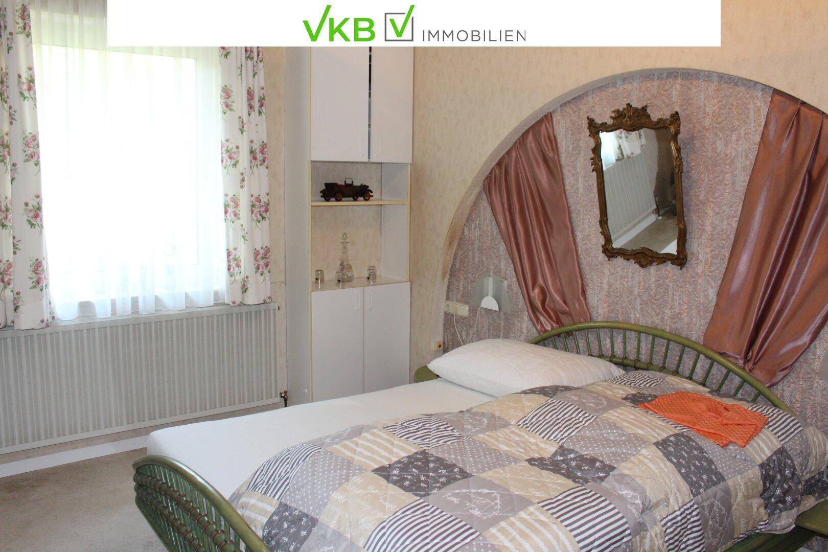 Gemütliches Schlafzimmer mit Doppelbett, floralen Vorhängen und einem dekorativen Spiegel.