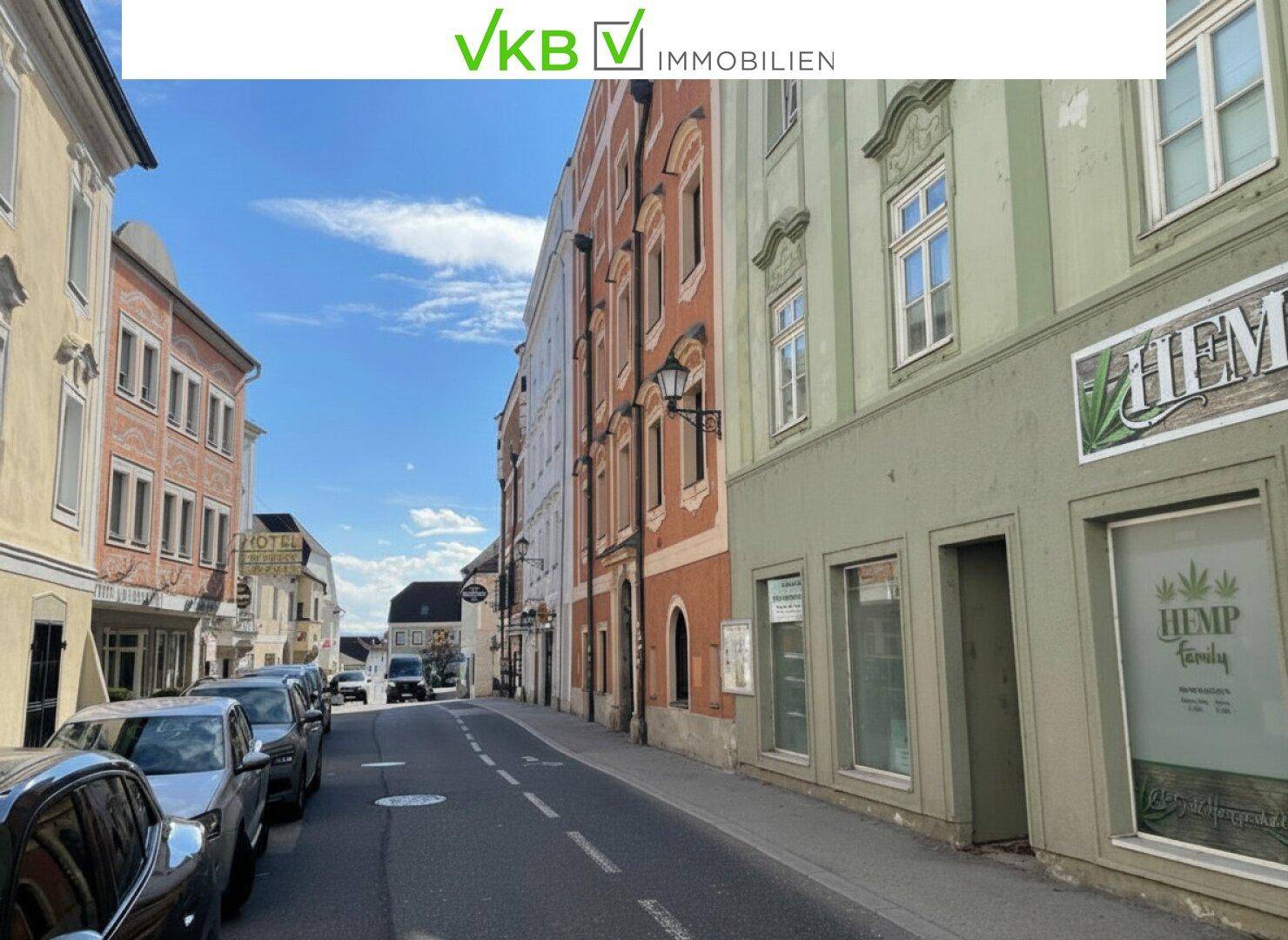 Eine belebte Straße mit historischen Gebäuden und geparkten Autos unter blauem Himmel.