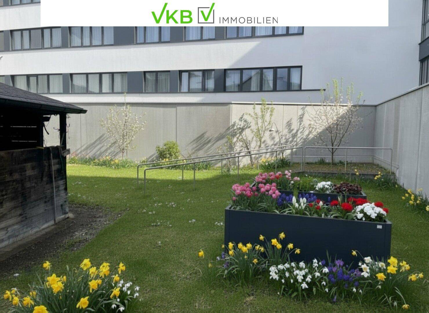 Gepflegter Gartenbereich mit bunten Blumenbeeten, Rasenfläche und einer Rollstuhlrampe im Hintergrund.