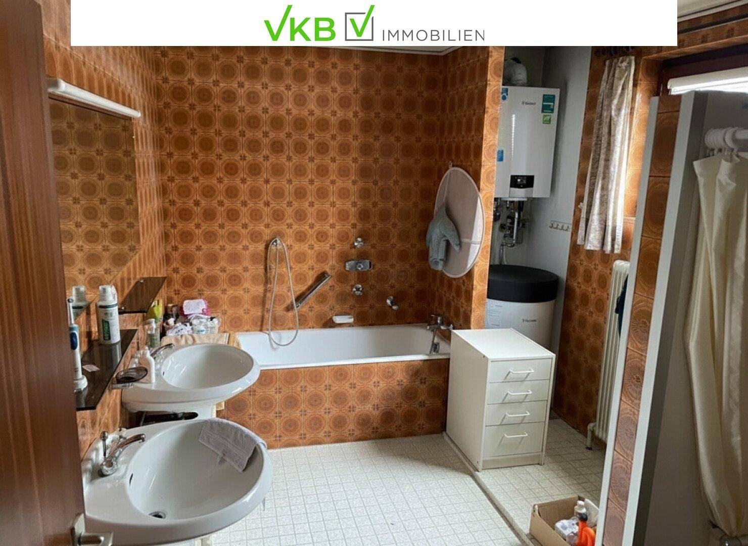 Badezimmer im Stil der 80er Jahre mit braunen Fliesen, Badewanne und zwei Waschbecken.