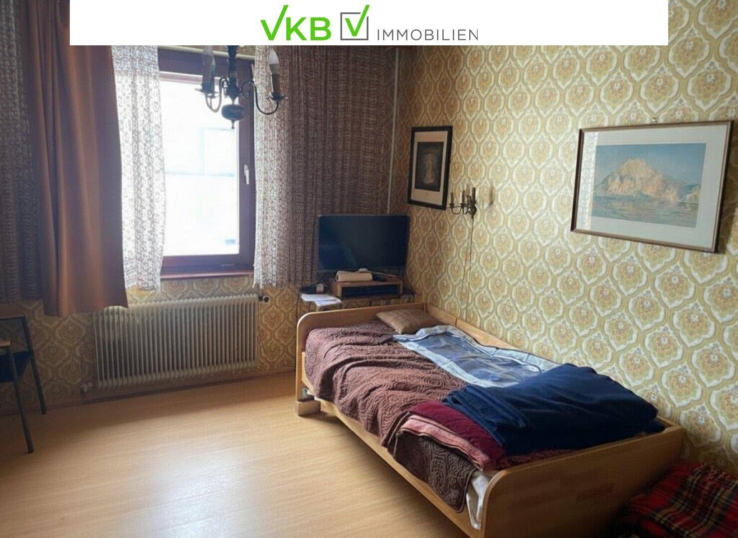 Schlafzimmer mit Einzelbett, gemusterter Tapete und Fenster für natürliches Licht.