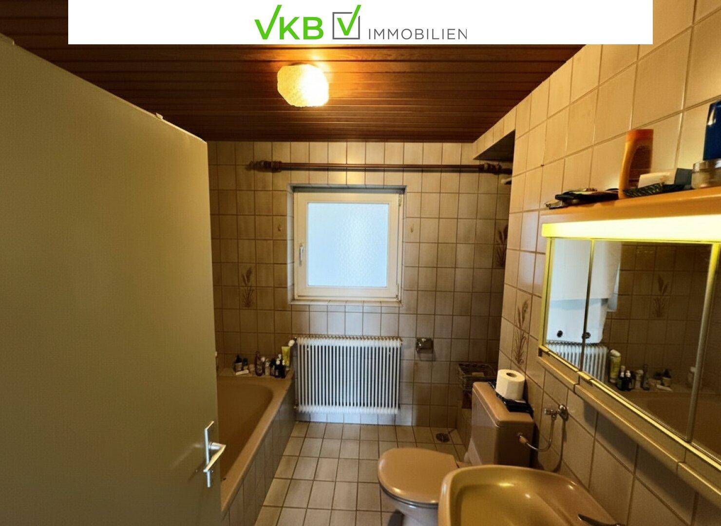 Badezimmer mit braunen Fliesen, Badewanne, WC und Fenster.