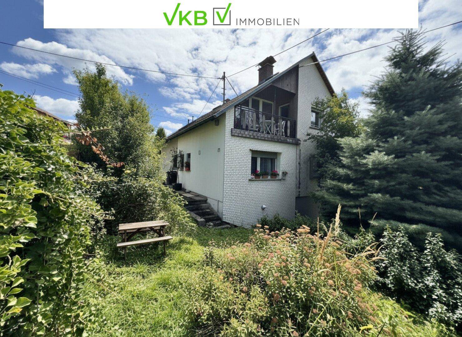 Gartenbereich mit einer Holzbank und üppiger Vegetation neben dem Haus.