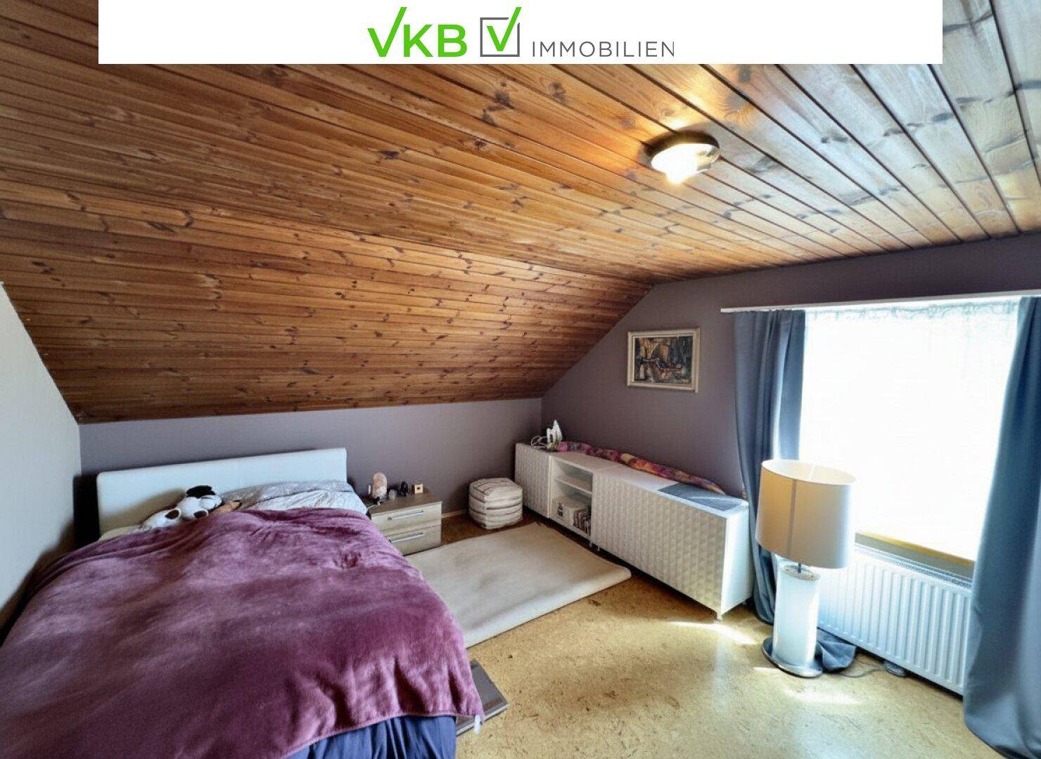 Schlafzimmer mit Holzdecke, Dachschräge, Doppelbett und Teppich.