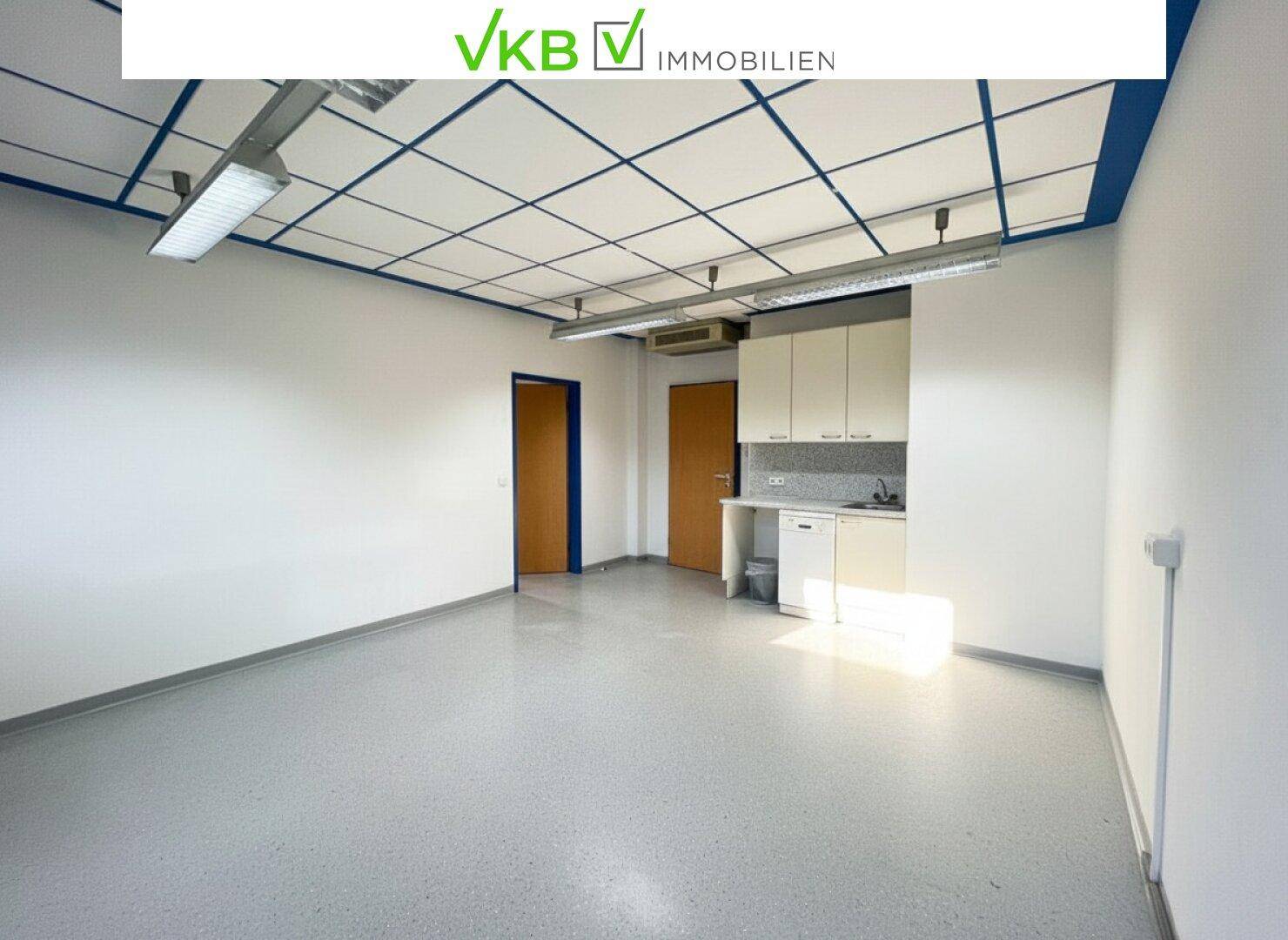Geräumiger, leerer Büroraum mit integrierter Küchenzeile und funktionaler Deckenbeleuchtung.