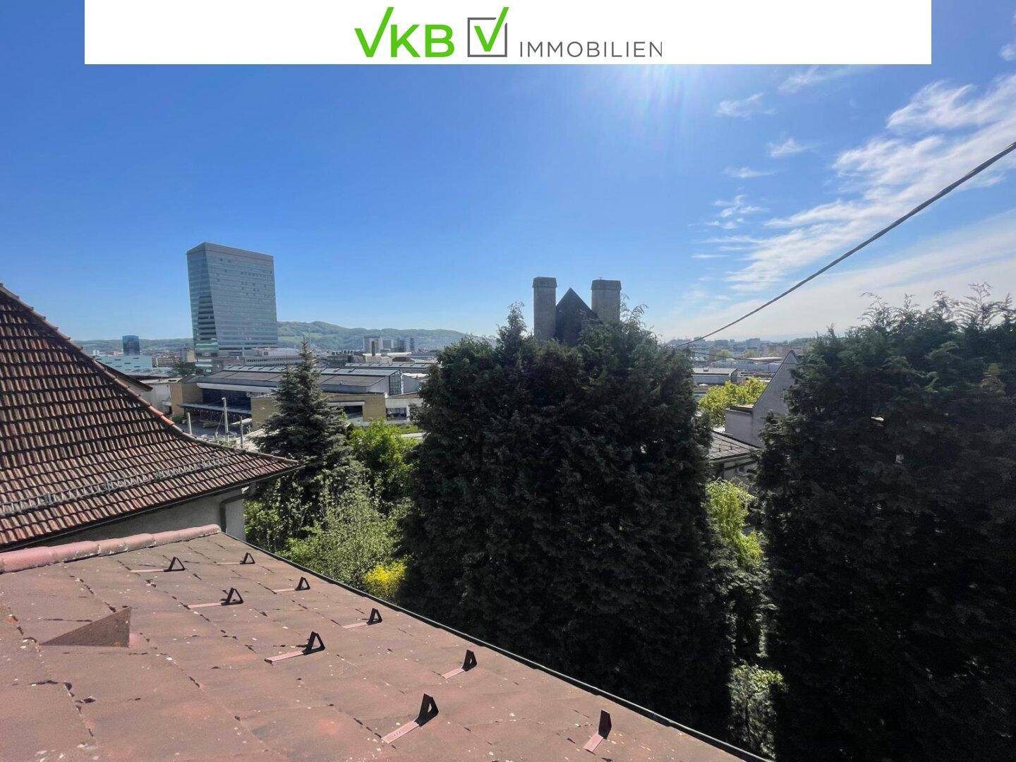 Panoramablick über die Stadt mit modernen Gebäuden und Dächern im Vordergrund.