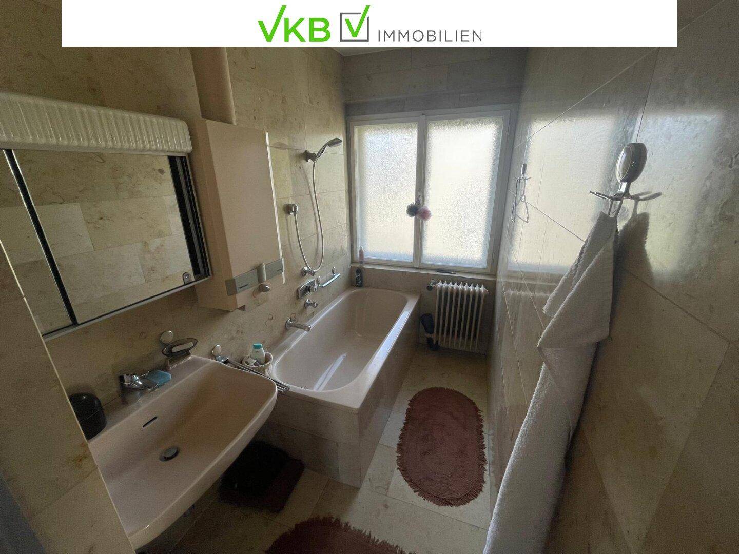 Badezimmer mit Badewanne, Waschbecken, Spiegelschrank und Fenster für Tageslicht.