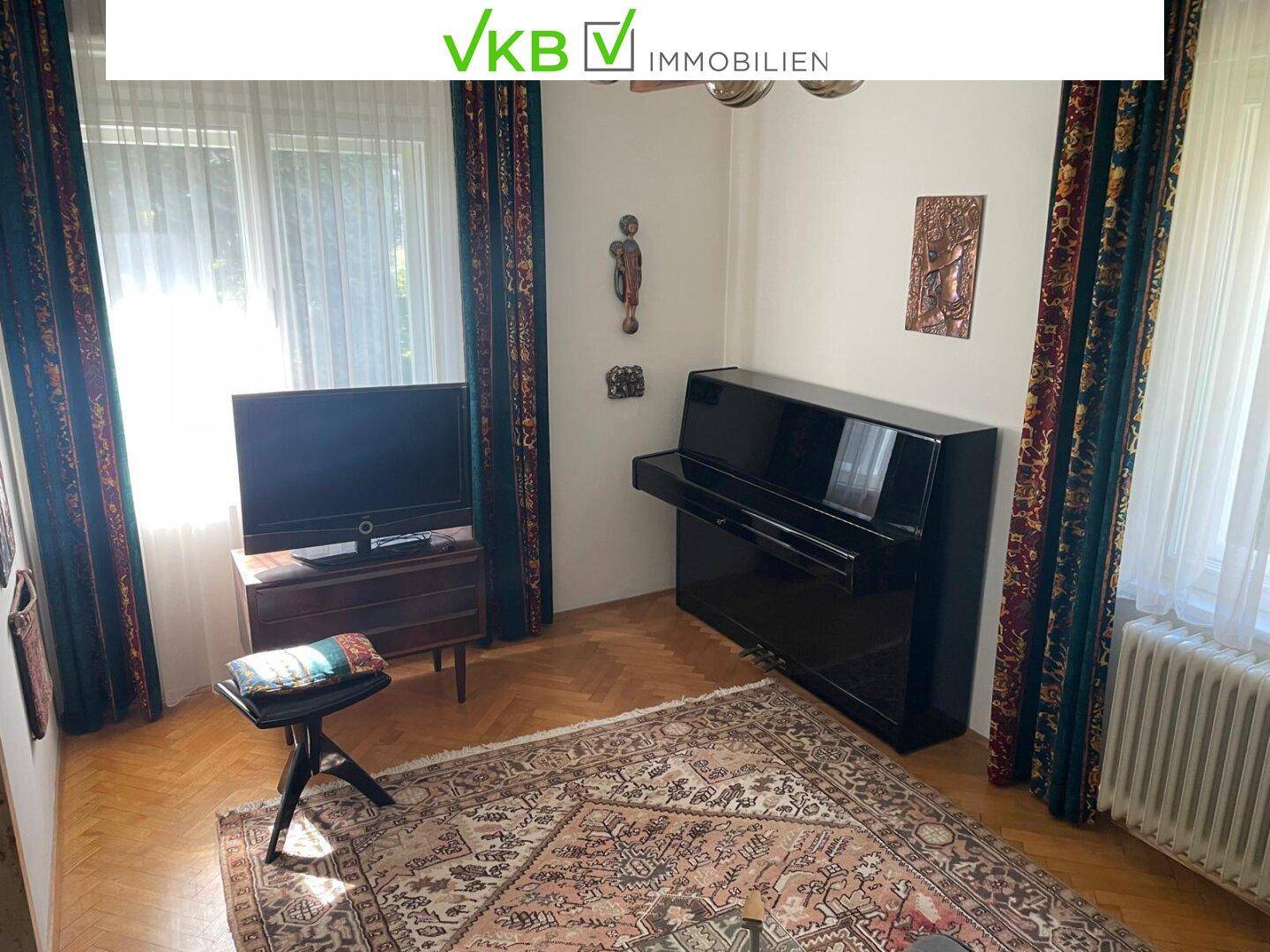 Wohnzimmer mit Klavier, Teppichboden und großen Fenstern für viel Tageslicht.